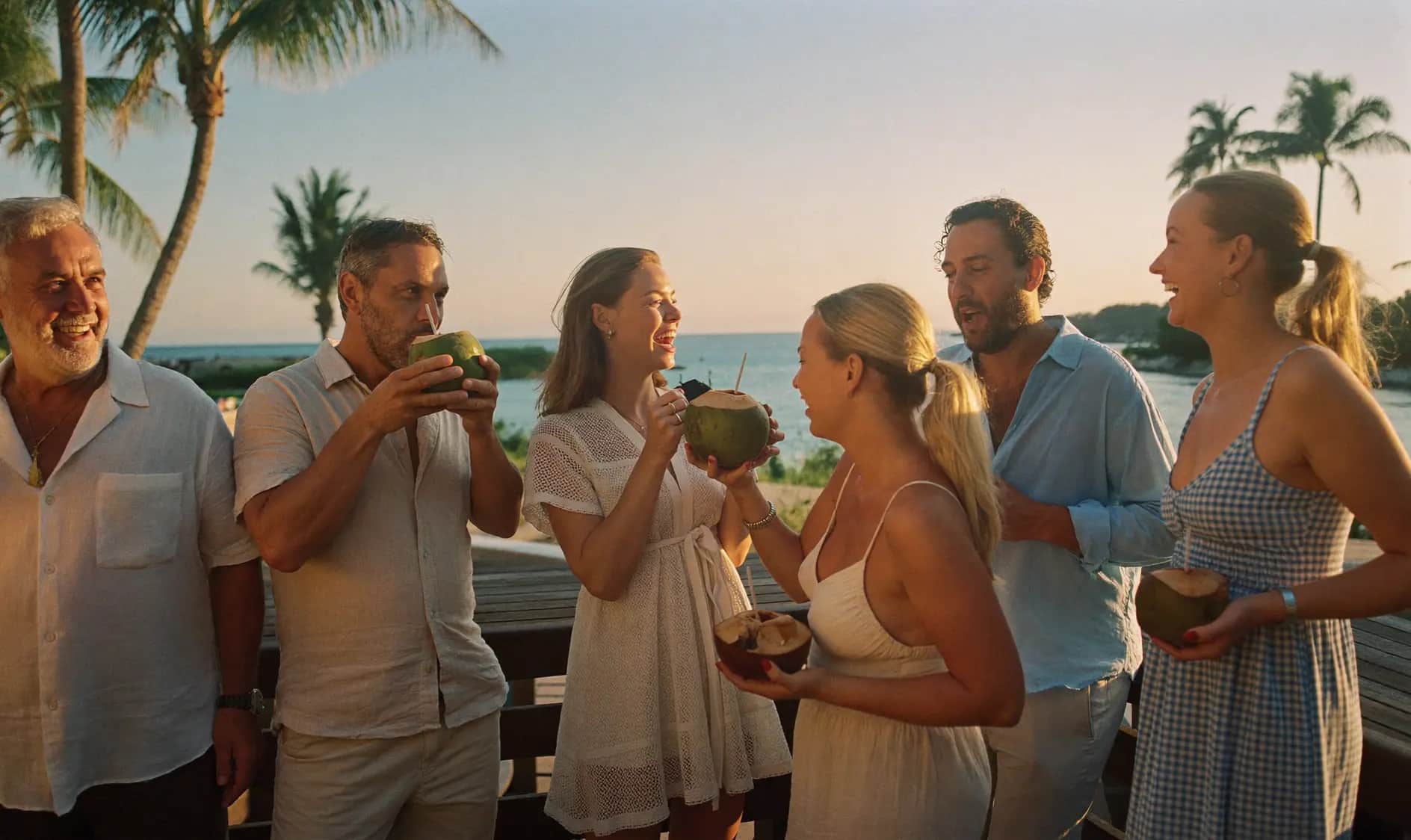 Eine Gruppe von Retreat-Gästen lacht gemeinsam mit frischen Kokosnüssen bei Sonnenuntergang auf einer Terrasse in Phuket