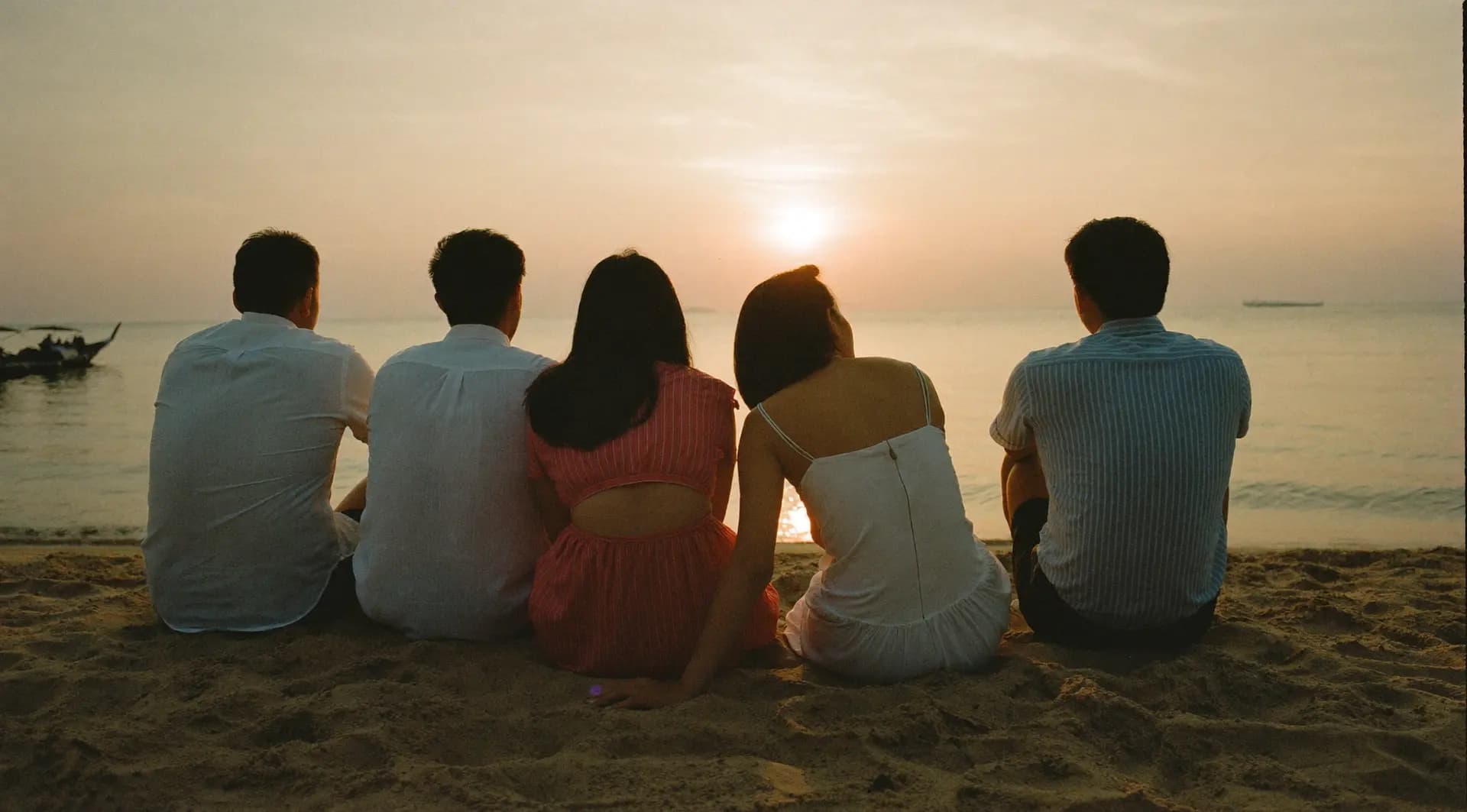 Eine kleine Gruppe sitzt eng beieinander im Sand und schaut auf den Sonnenuntergang über dem Meer
