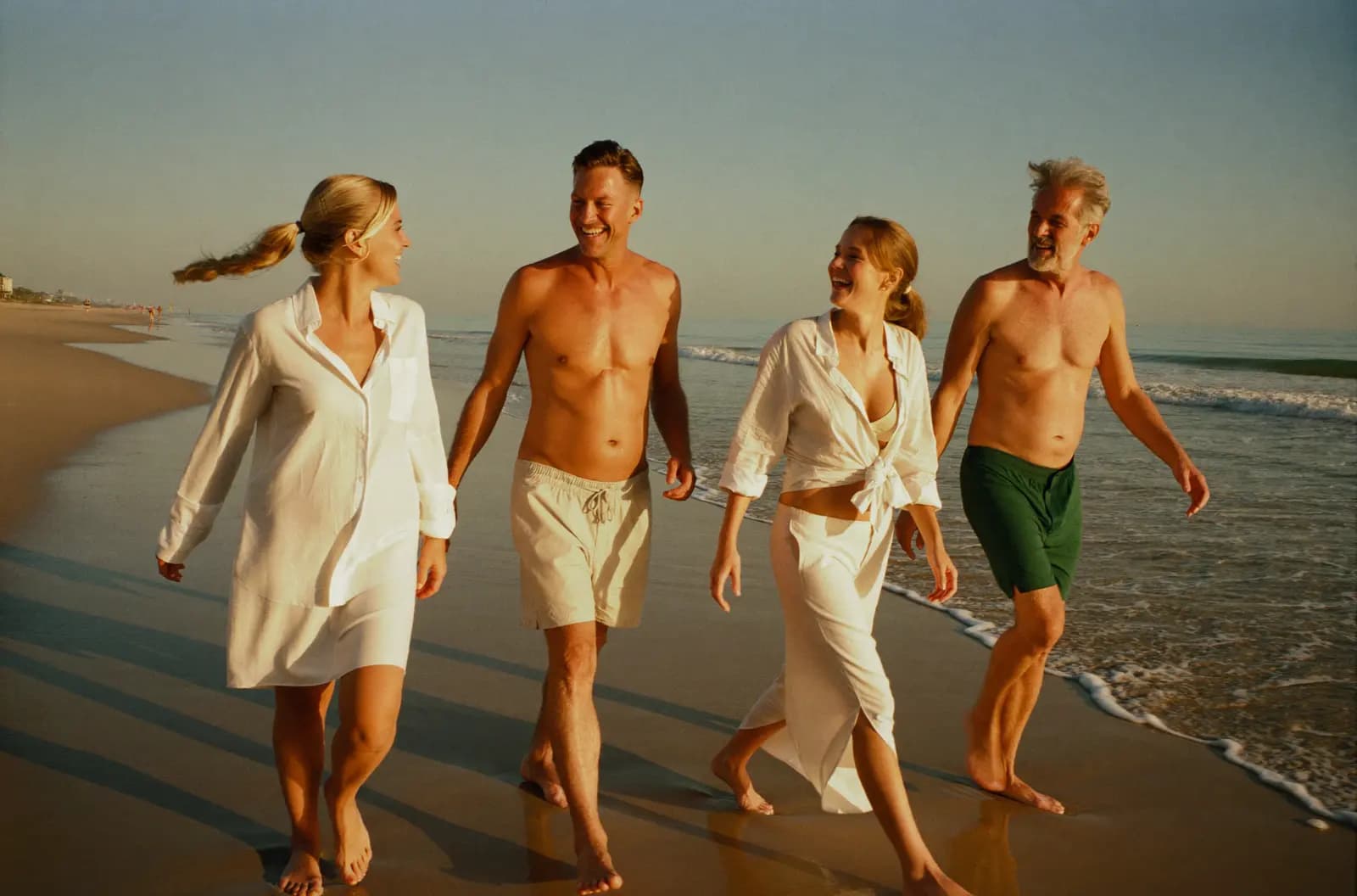 Vier Retreat-Gäste spazieren lachend barfuß bei Sonnenuntergang am Strand entlang