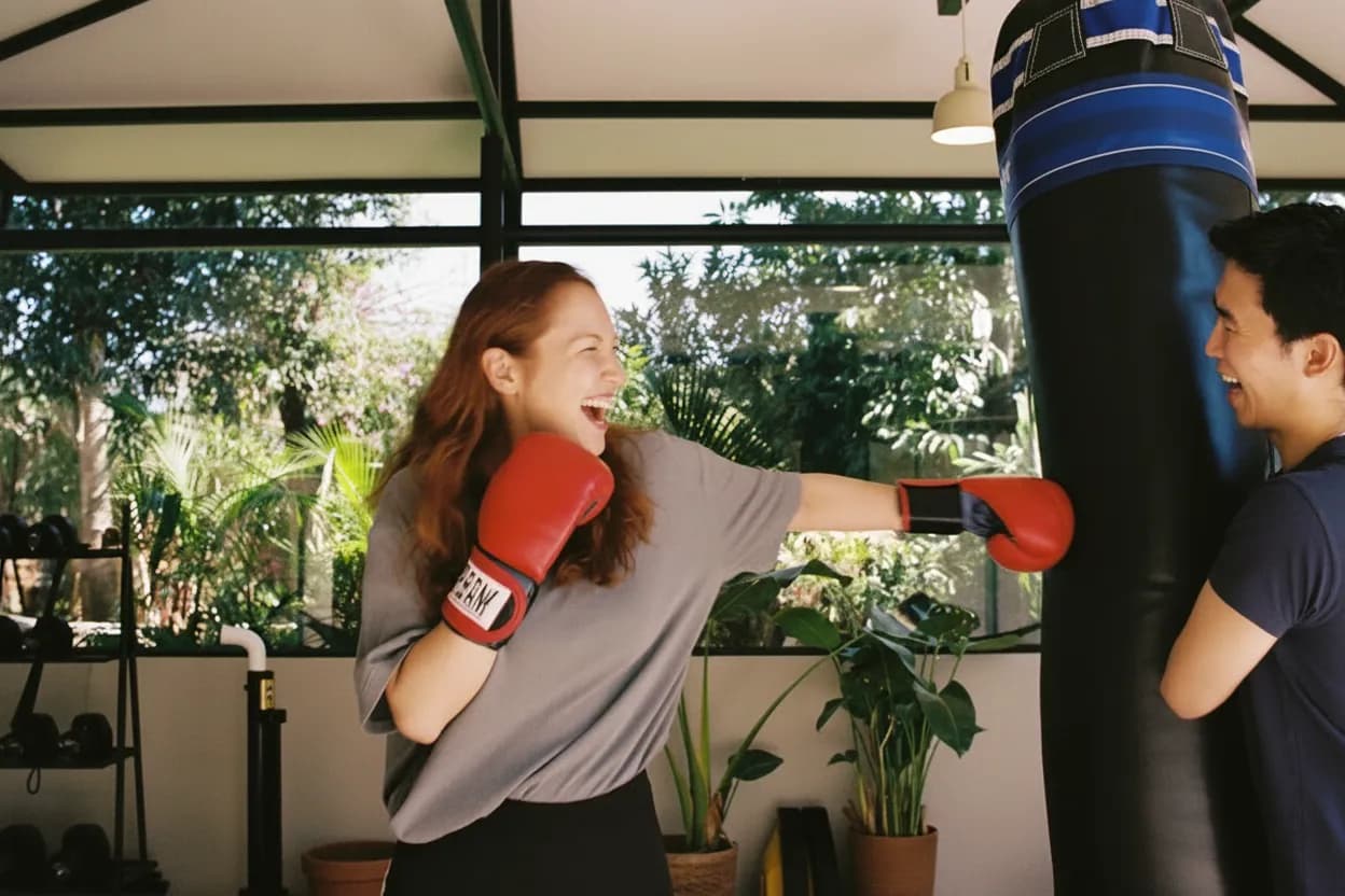 Eine Frau trainiert lachend an den Pratzen eines Thai-Trainers, daneben ein Mann, der grinsend verschnauft